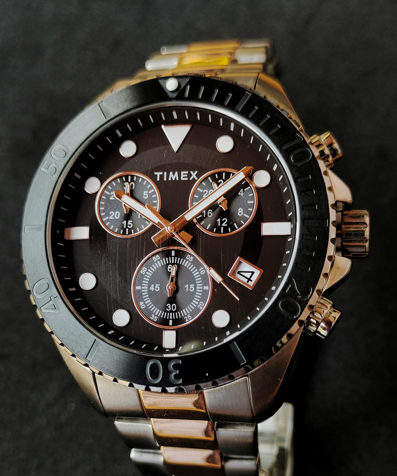 Steel and rose-gold chronograph diver with a black dial and bezel against a dark background